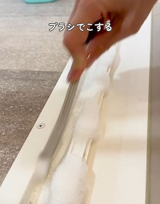 浴室のドアレールをブラシでこすり洗いしている様子