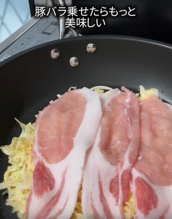 フライパンに広げた具材の上に豚バラ肉をのせる様子