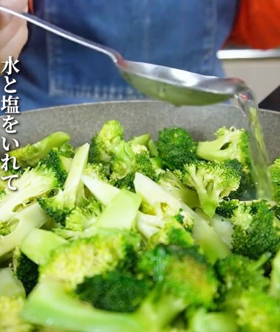 ブロッコリーを炒めているフライパンに計量スプーンで水を加える様子