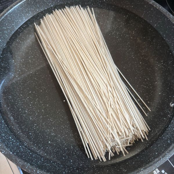 水を入れた鍋にそばを入れた様子