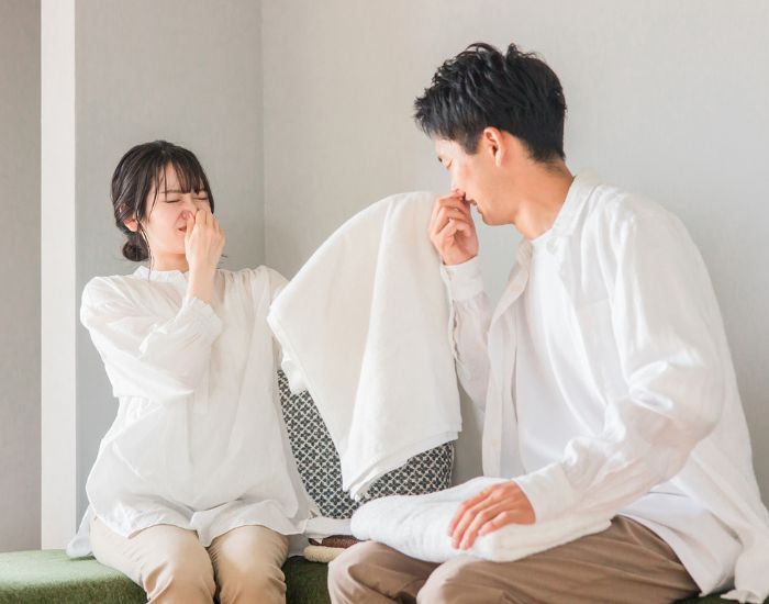 タオル臭いを嗅いで鼻をつまんでいる男女の写真