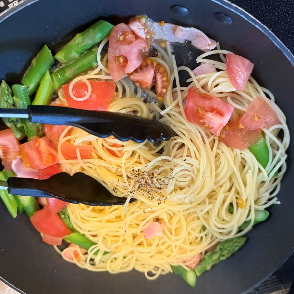 パスタと具材を混ぜ合わせたフライパンに塩コショウをした様子