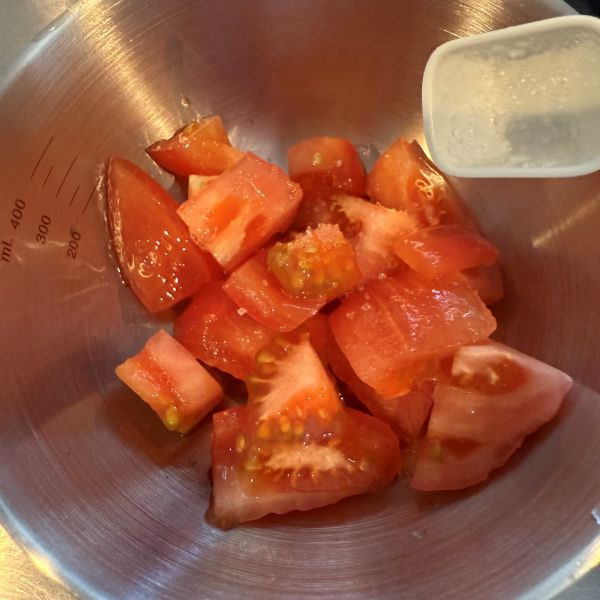 カットしたトマトをボウルに入れて塩を振る様子
