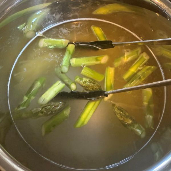 パスタとカットしたアスパラガスを鍋でゆでる様子