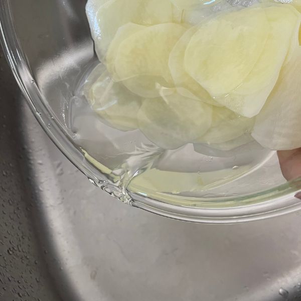 スライスしたジャガイモが入ったボウルの水を捨てる様子