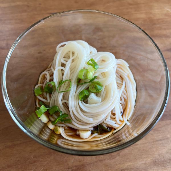 解凍したそうめんを小皿に盛りつけてつゆとネギをかけた様子