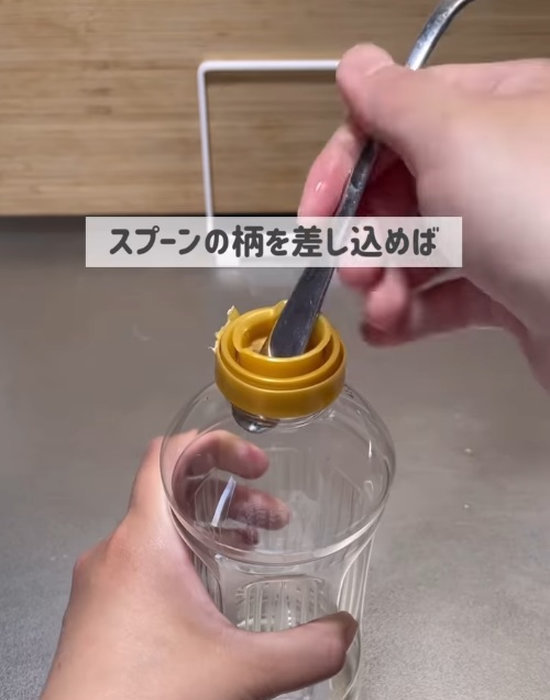 調味料用ペットボトルの中栓の穴にスプーンの柄を差し込む様子