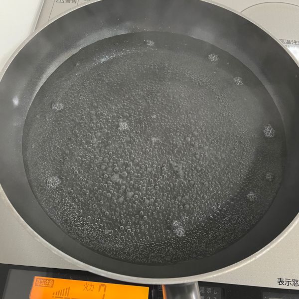 大きめのフライパンに水を張って火にかける様子