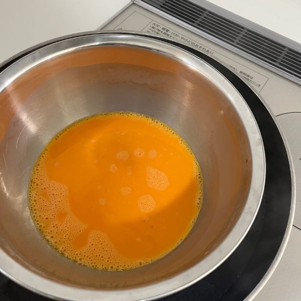 お湯の沸騰したフライパンに卵を溶いたボウルを入れて湯せんする様子