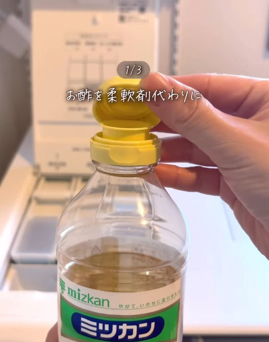 洗濯機の前で酢のボトルの蓋を開けている様子