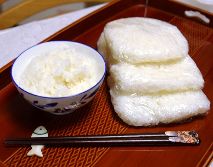 お茶碗に入ったご飯とラップで小分けにしたご飯をおぼんの上に並べて置いている様子