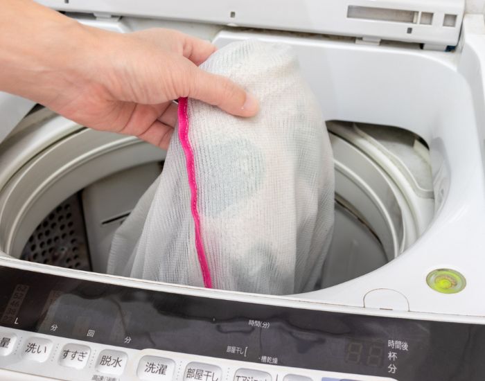 洗濯用ネットに入れた洗濯物を洗濯機に入れる様子