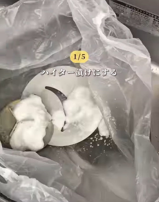 ゴミ袋に入った排水口のパーツにキッチンハイターをスプレーした様子