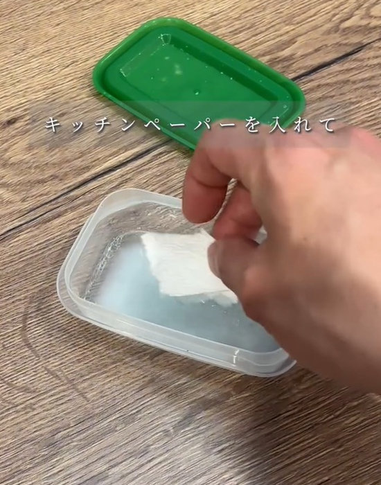 食器用洗剤が入った保存容器にキッチンペーパーを入れている様子