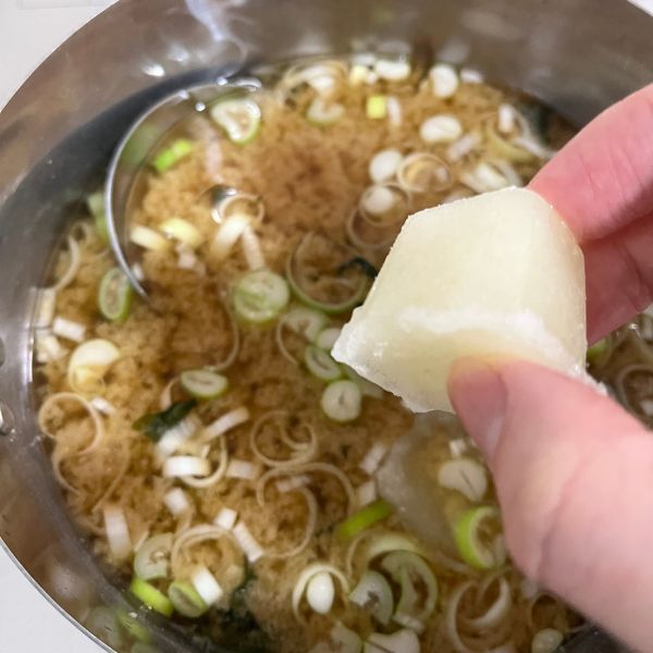 味噌汁の入った鍋の上で凍ったタマネギペーストを手に持っている様子