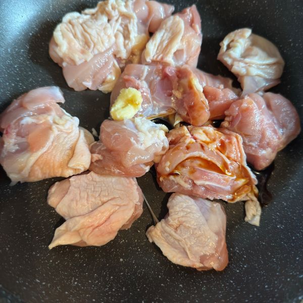 フライパンに入れた鶏肉におろししょうがと醤油をかけた様子