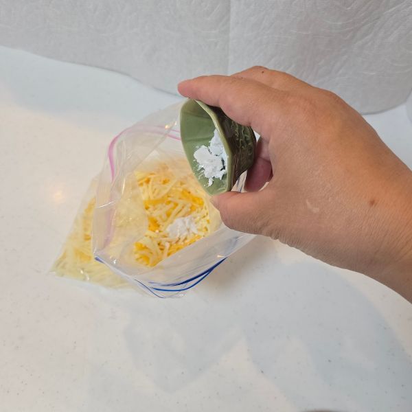 冷凍用保存袋に入れたピザ用チーズに片栗粉をかける様子