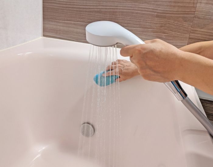 シャワーの水を当てながら浴槽をスポンジで洗う様子
