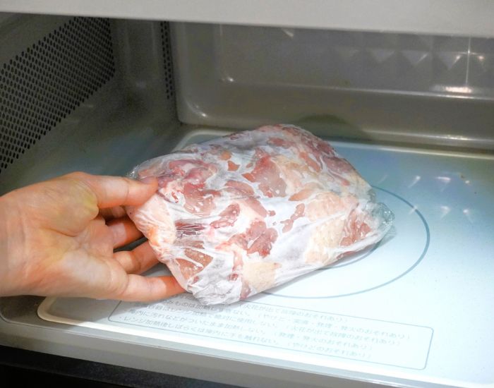 電子レンジにラップで包んだ冷凍肉を入れる様子
