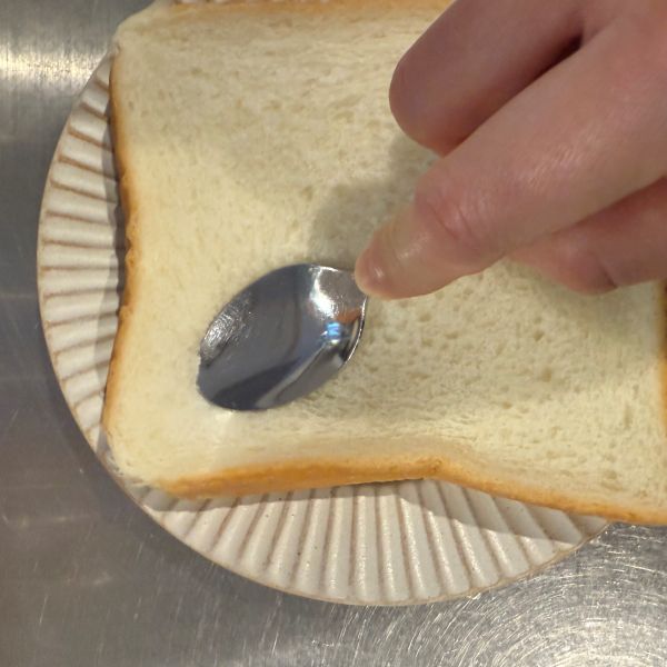 スプーンのすくう部分を食パンに押し付ける様子