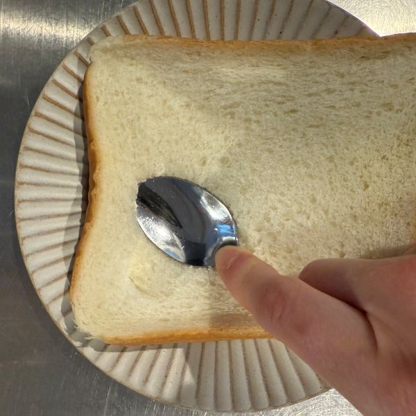 食パンに対してスプーンを斜めに押し付けてハートの形を作る様子