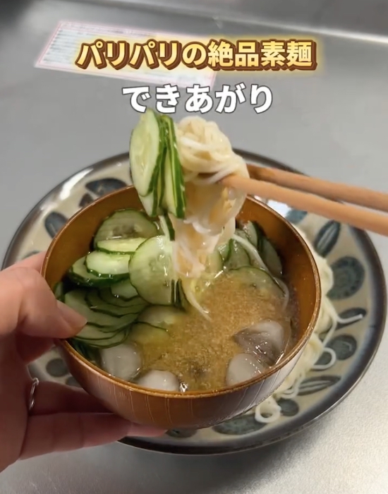 キュウリとすりゴマの入った麺つゆにそうめんを入れる様子