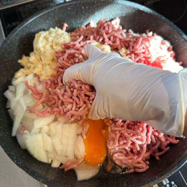 調理用の手袋を着けてフライパンに入れたハンバーグの材料をこねる様子