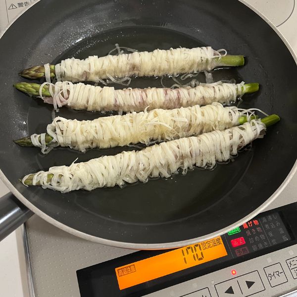 油を入れたフライパンに春巻きの皮を巻いたアスパラガスを入れて揚げ焼きにする様子