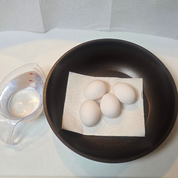 卵を入れたフライパンと水を入れた計量カップを並べた様子