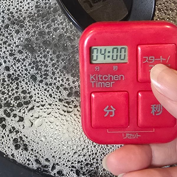 卵と水を入れたフライパンにふたをしてキッチンタイマーで４分測る様子