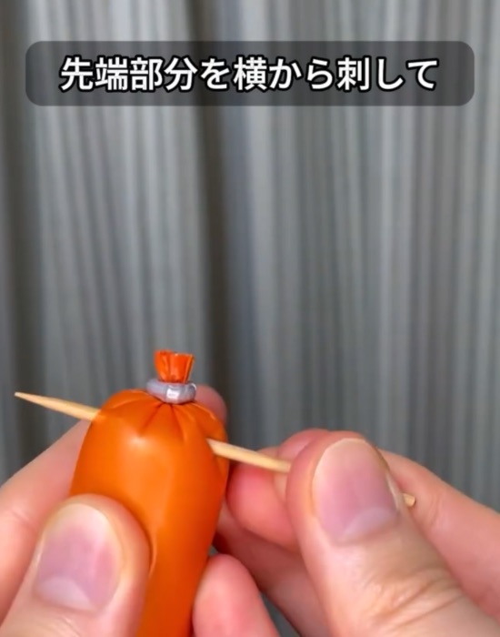 つまようじを魚肉ソーセージの先端に刺して貫通させる様子
