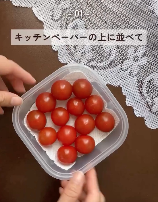 キッチンペーパーを敷いた保存容器の中にミニトマトを入れる様子