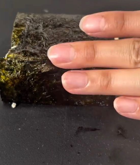 豆腐を巻いたのりの巻き終わりを手で押さえる様子