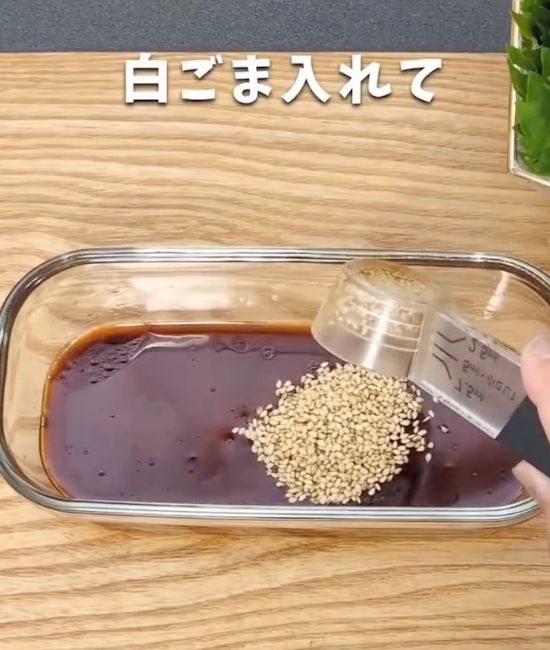 調味料を入れた耐熱容器に計量スプーンで白ごまを入れる様子