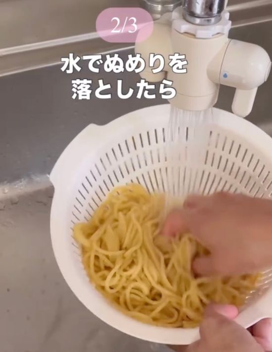 ゆでたパスタをザルにあげて流水で洗う様子