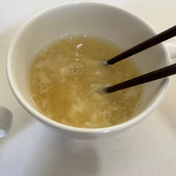 卵白と鶏がらスープのもとが入ったカップにお湯を注いで箸で混ぜる様子