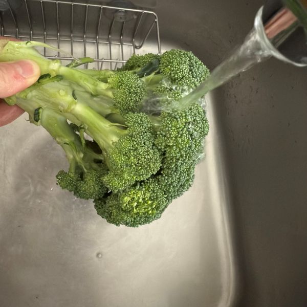 ブロッコリーの茎を持って水道水で洗う様子