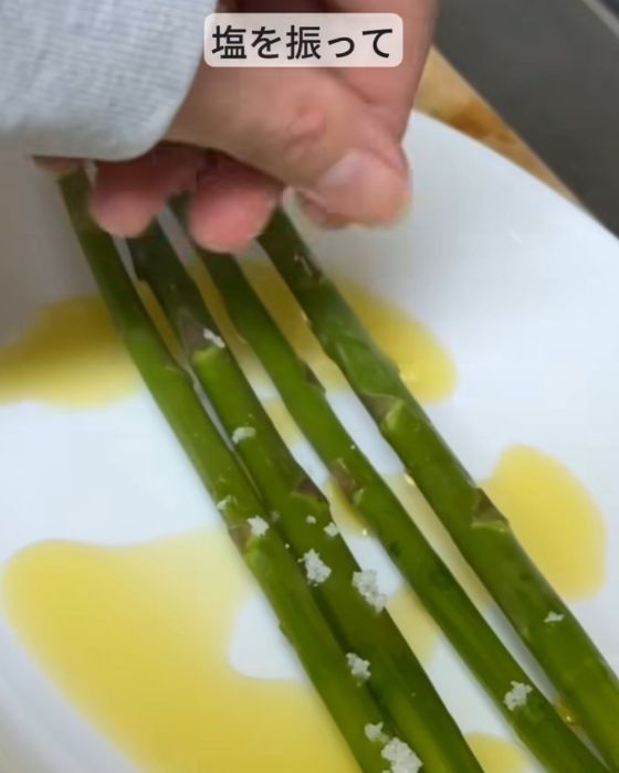 オリーブオイルをかけたアスパラガスに塩を振る様子