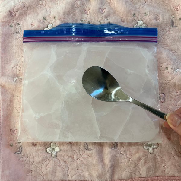 ジッパー付き保存袋に水を入れて凍らせた氷をスプーンの背で叩き割る様子