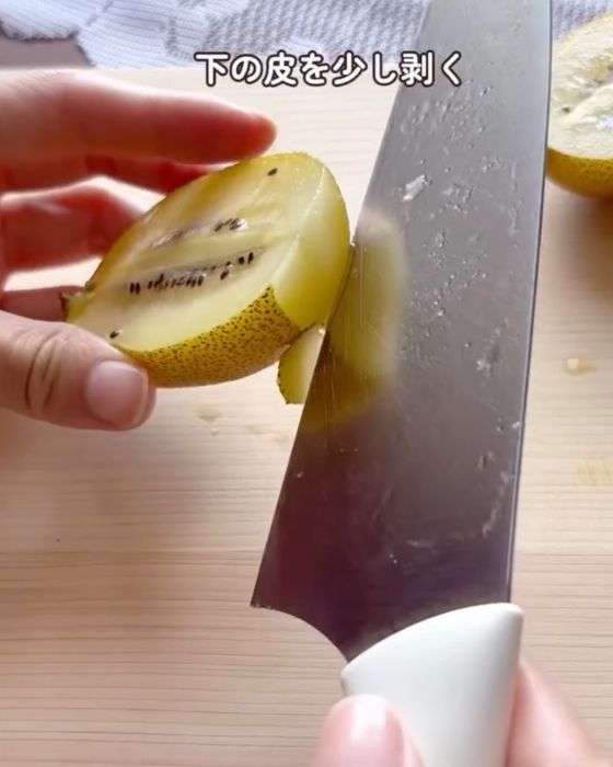 半分に切ったキウイの下の部分の皮を包丁で少しだけむく様子