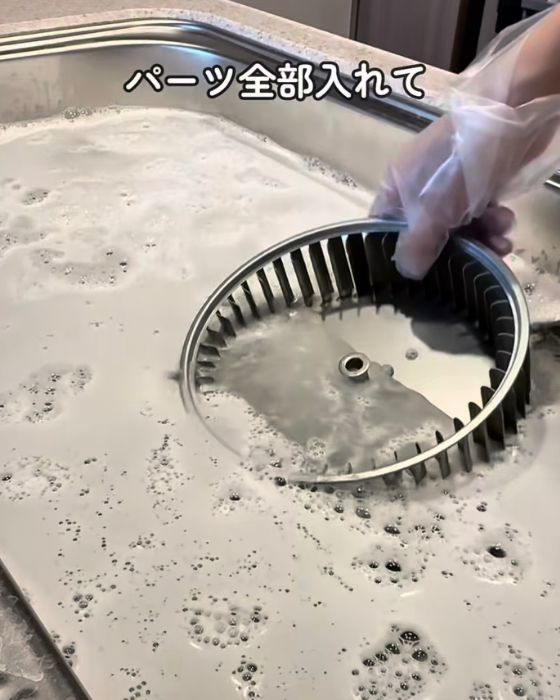 シンクにためた洗剤を溶かしたお湯に換気扇のパーツを入れる様子