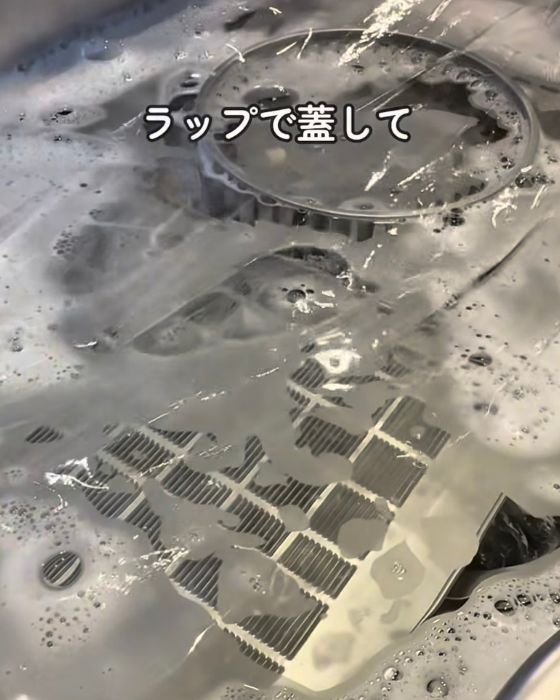 シンクにためたお湯に換気扇のパーツを入れて表面にラップをかけた様子