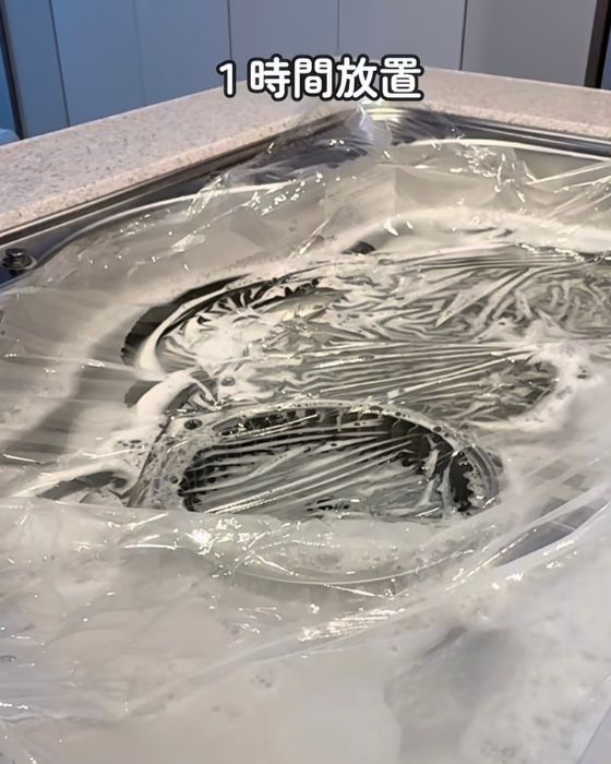 シンクに洗剤を溶かしたお湯と換気扇のパーツを入れてシンクを覆うようにラップをかけた様子