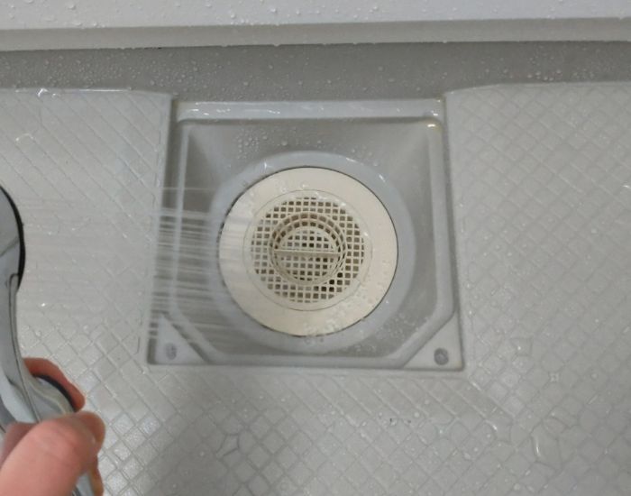 浴室の排水口の蓋を開けてシャワーをかける様子