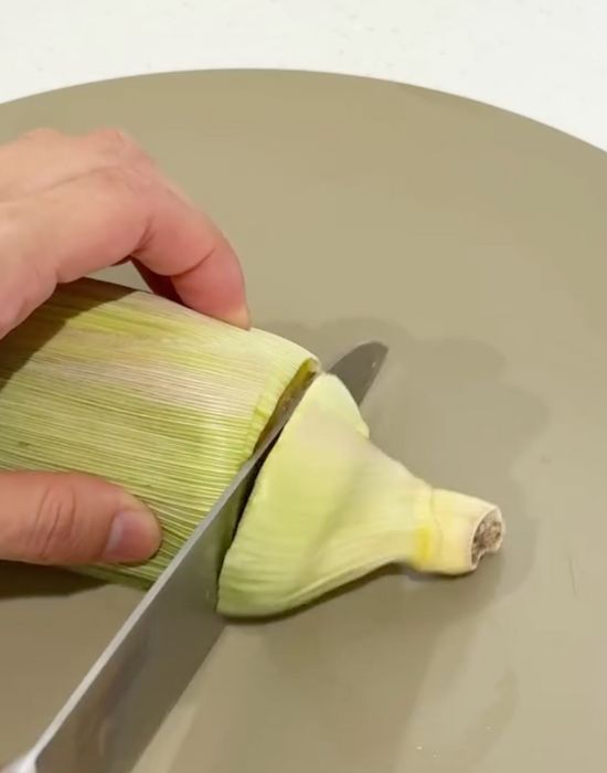 加熱したトウモロコシの根元を皮ごと包丁で切る様子
