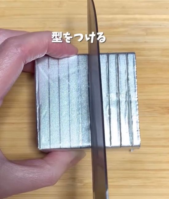 バターの銀紙の上から目盛り線に合わせて包丁で切り込みを入れる様子