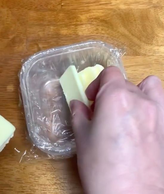 ラップを敷いた保存容器にカットしたバターを入れる様子