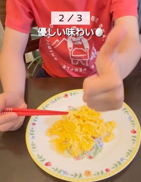 皿にのせられたスクランブルエッグを前に子供がグッドサインを向ける様子
