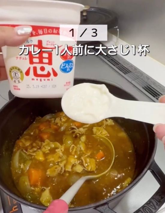 鍋に入ったカレーにヨーグルトを大さじ一杯加えようとしている様子