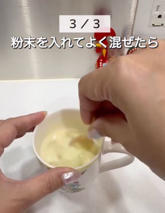 マグカップに加熱した牛乳と粉末コーンスープを入れてスプーンで混ぜる様子